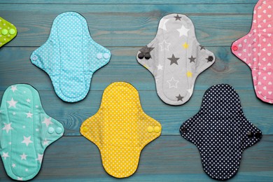 Many reusable cloth menstrual pads on light blue wooden table, flat lay