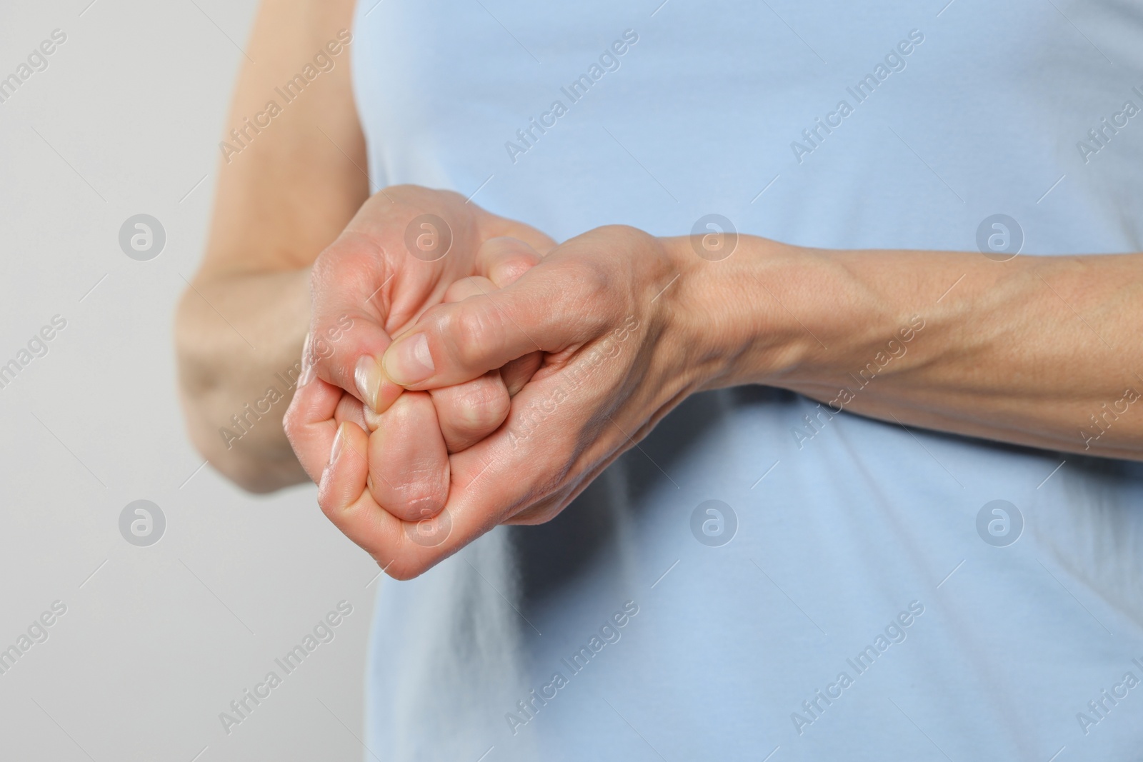 Photo of Woman cracking her knuckles on light grey background, closeup. Bad habit