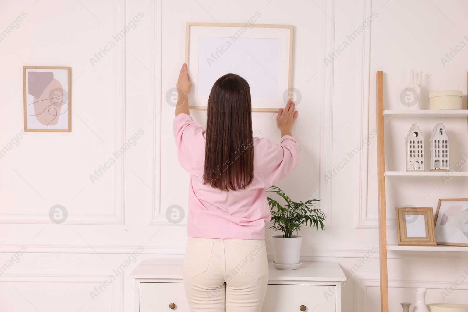 Photo of Woman hanging picture frame on white wall at home, back view