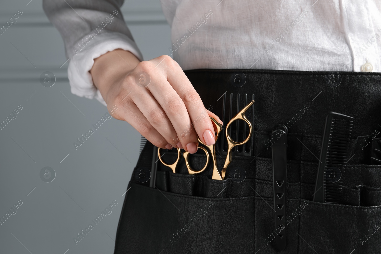 Photo of Hairstylist with professional tools in waist pouch near grey wall, closeup