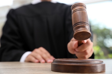 Photo of Judge with gavel at wooden table indoors, closeup. Criminal law