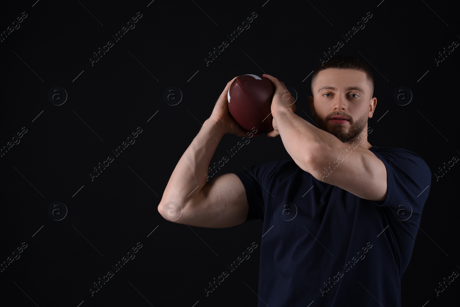 Photo of Athletic young man with American football ball on black background. Space for text