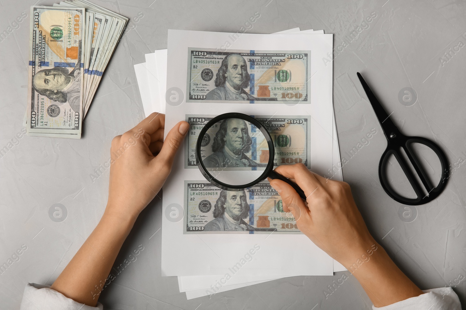 Photo of Counterfeiter examining sheet of paper with dollar banknotes at grey table, top view. Fake money concept