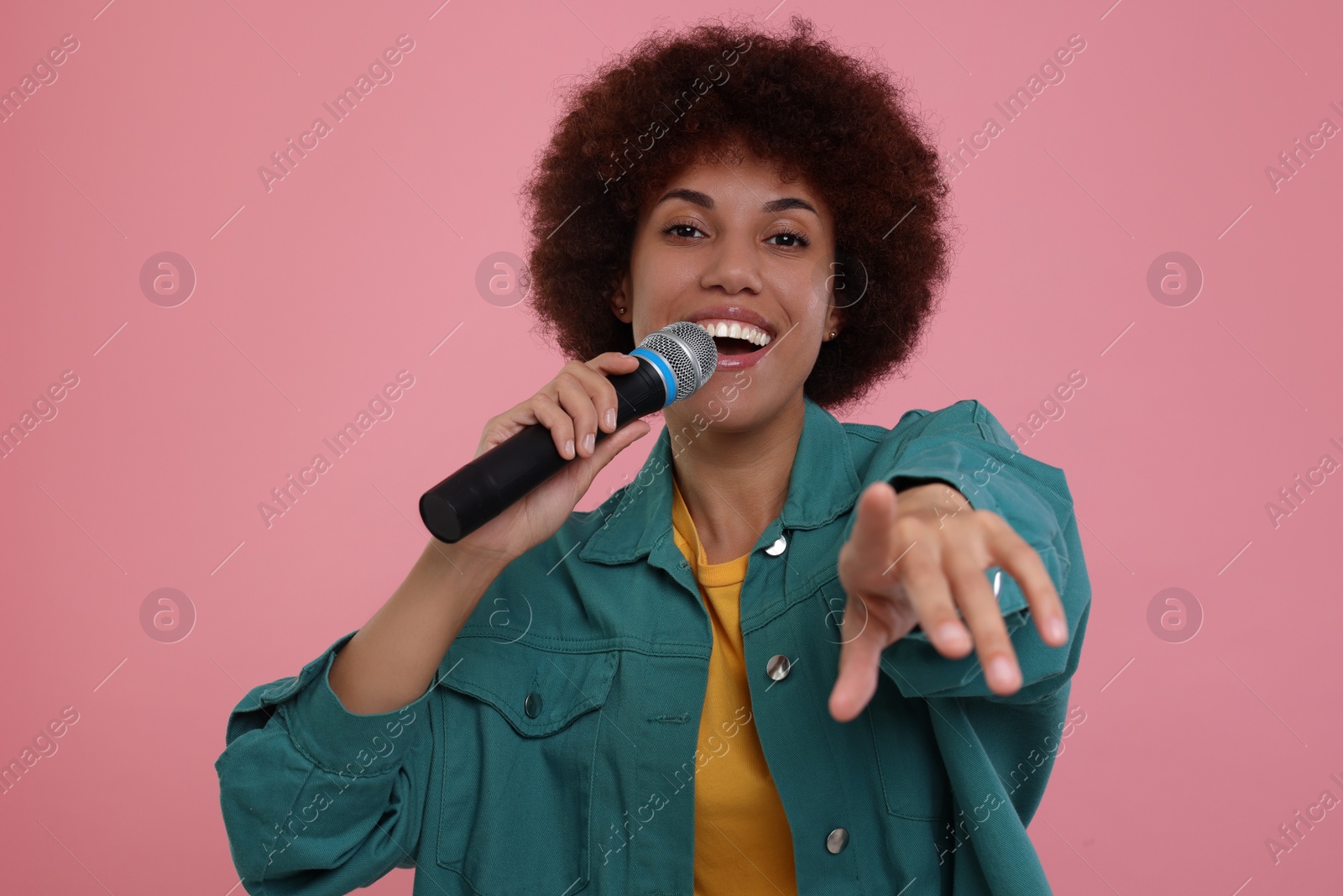 Photo of Curly young woman with microphone singing on pink background