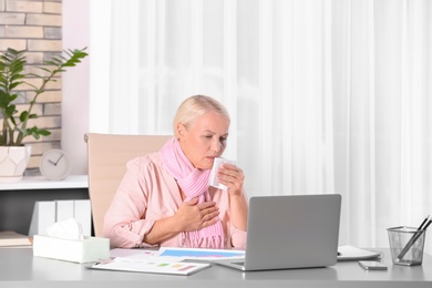 Photo of Ill mature woman suffering from cough at workplace