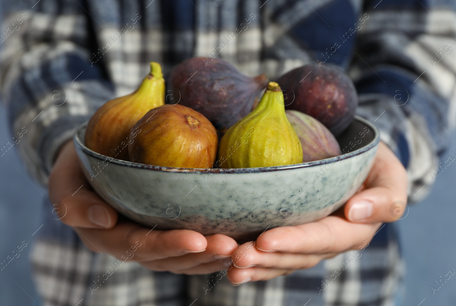 Photo of Woman holding bowl with tasty raw figs on light blue background, closeup