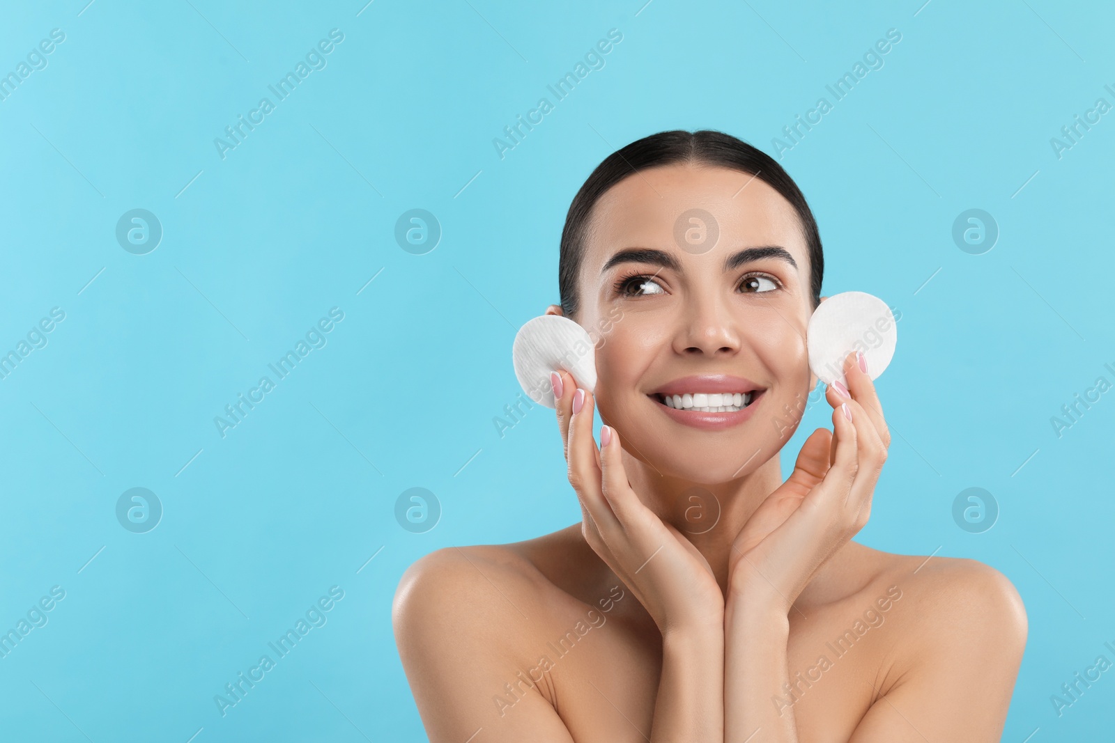 Photo of Beautiful woman holding cotton pads on light blue background, space for text. Removing makeup