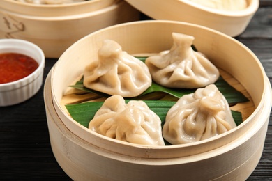 Bamboo steamer with leaves and tasty baozi dumplings on table