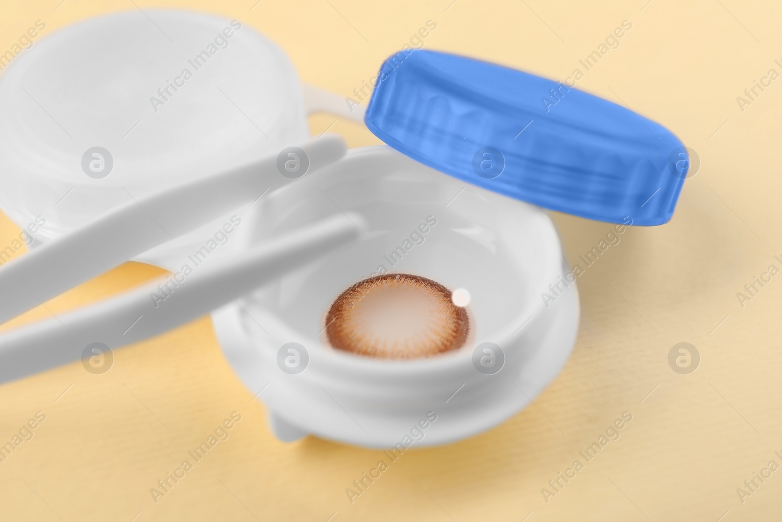 Photo of Case with color contact lenses and tweezers on pale yellow background, closeup