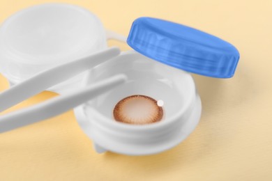 Case with color contact lenses and tweezers on pale yellow background, closeup