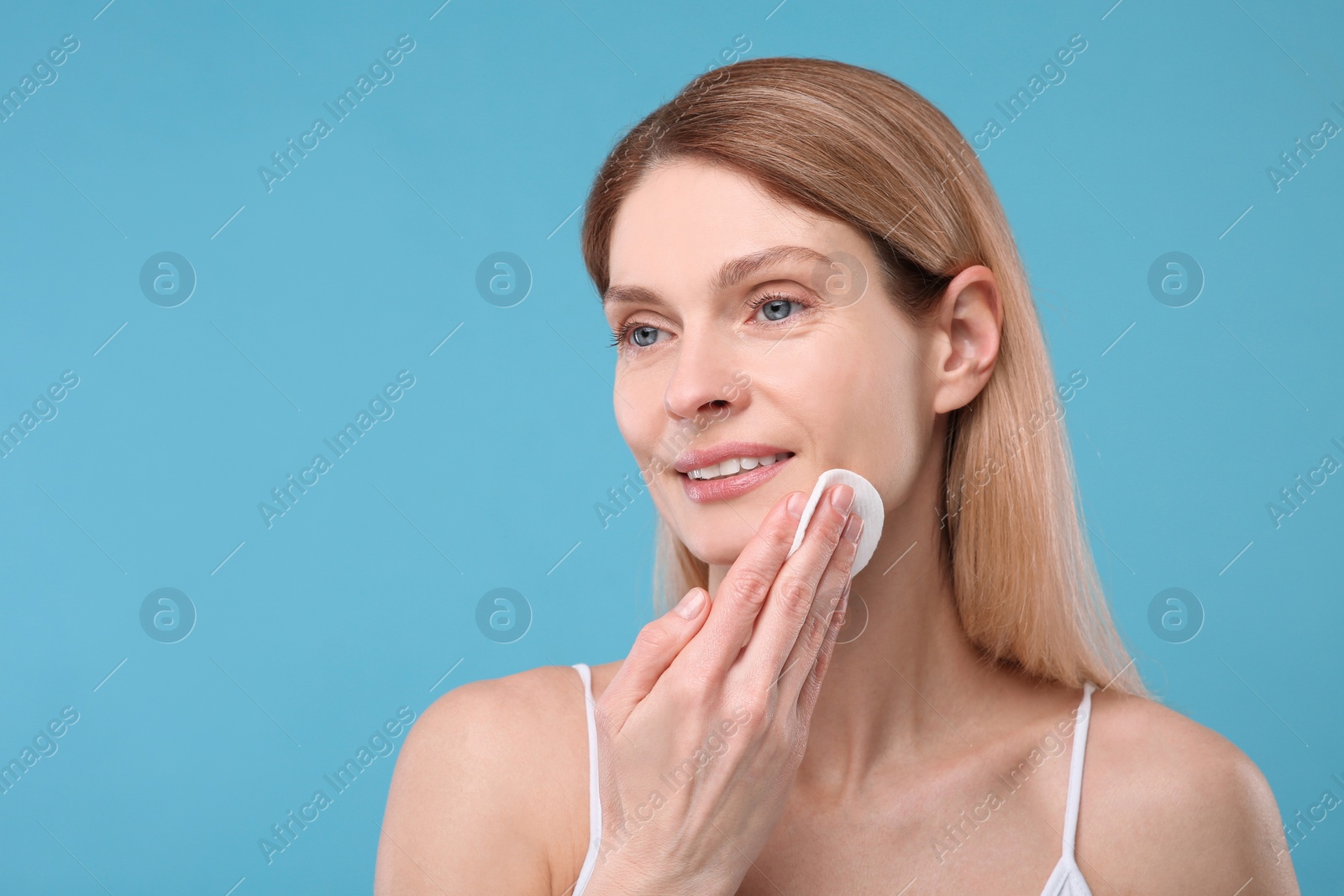 Photo of Beautiful woman removing makeup with cotton pad on light blue background, space for text