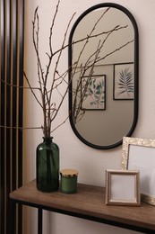 Photo of Beautiful tree twigs in vase and empty frames on wooden table near white wall indoors