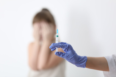 Doctor holding syringe with chickenpox vaccine and scared child on background, closeup. Varicella virus prevention