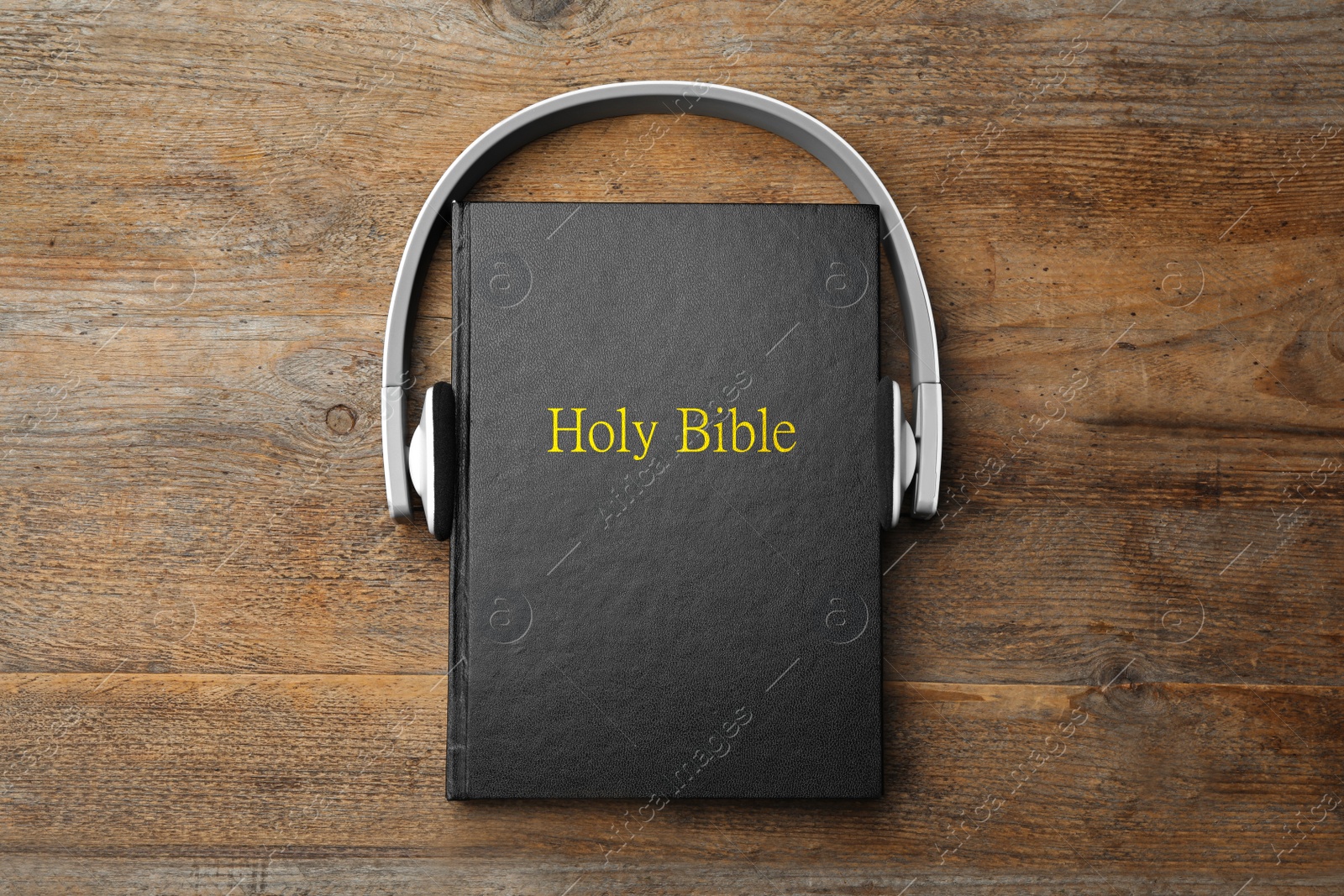 Photo of Bible and headphones on wooden background, top view. Religious audiobook