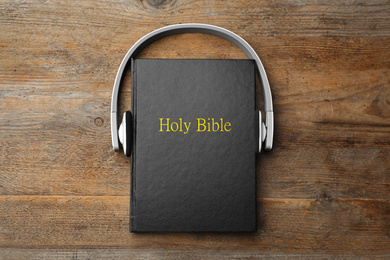Bible and headphones on wooden background, top view. Religious audiobook