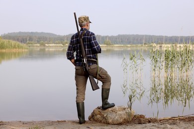 Photo of Man with hunting rifle near lake outdoors, back view