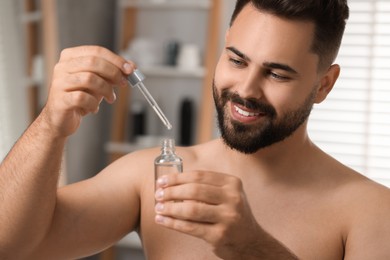 Photo of Handsome man with cosmetic serum in his hands in bathroom