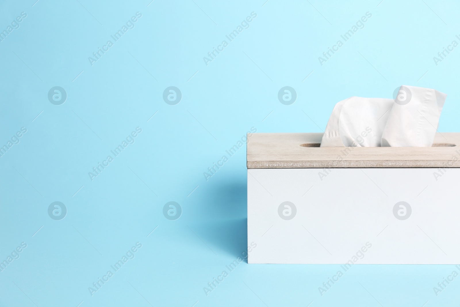 Photo of Holder with paper tissues on light blue background. Space for text