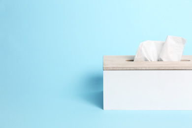 Photo of Holder with paper tissues on light blue background. Space for text