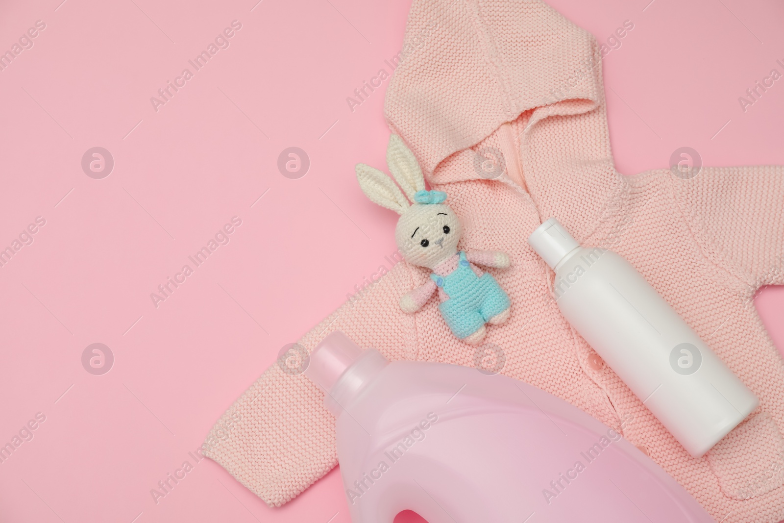 Photo of Bottles of laundry detergents, baby sweatshirt and toy bunny on pink background, flat lay. Space for text