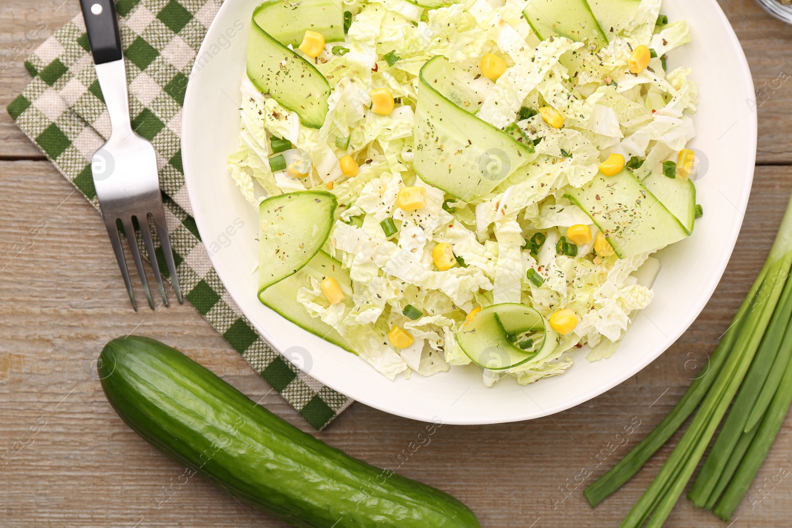 Photo of Tasty salad with Chinese cabbage in bowl and ingredients on wooden table, flat lay