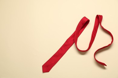 Red necktie on beige background, top view. Space for text