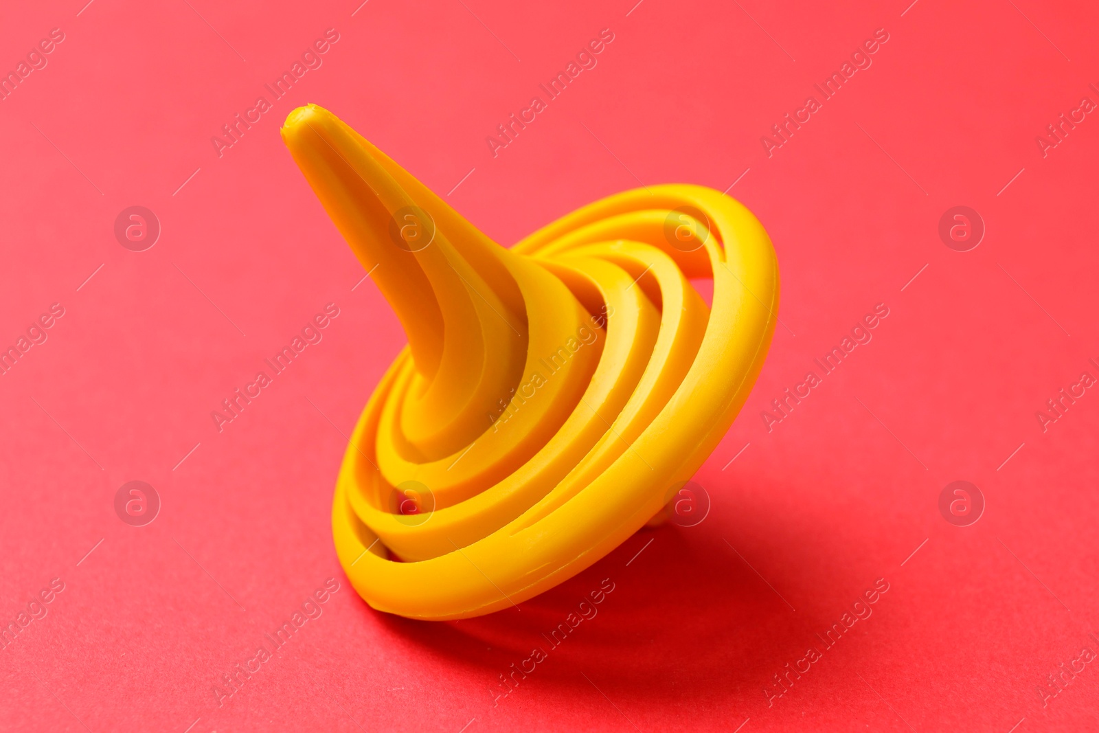 Photo of One yellow spinning top on red background, closeup