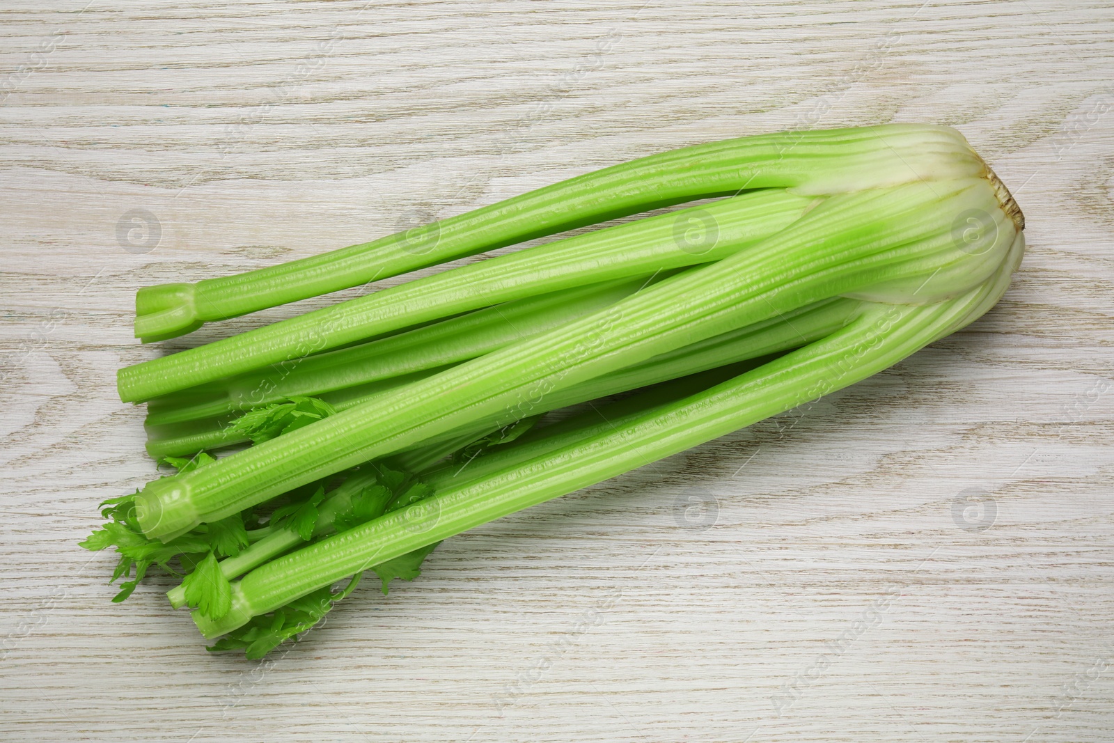 Photo of One fresh green celery bunch on white wooden table, top view