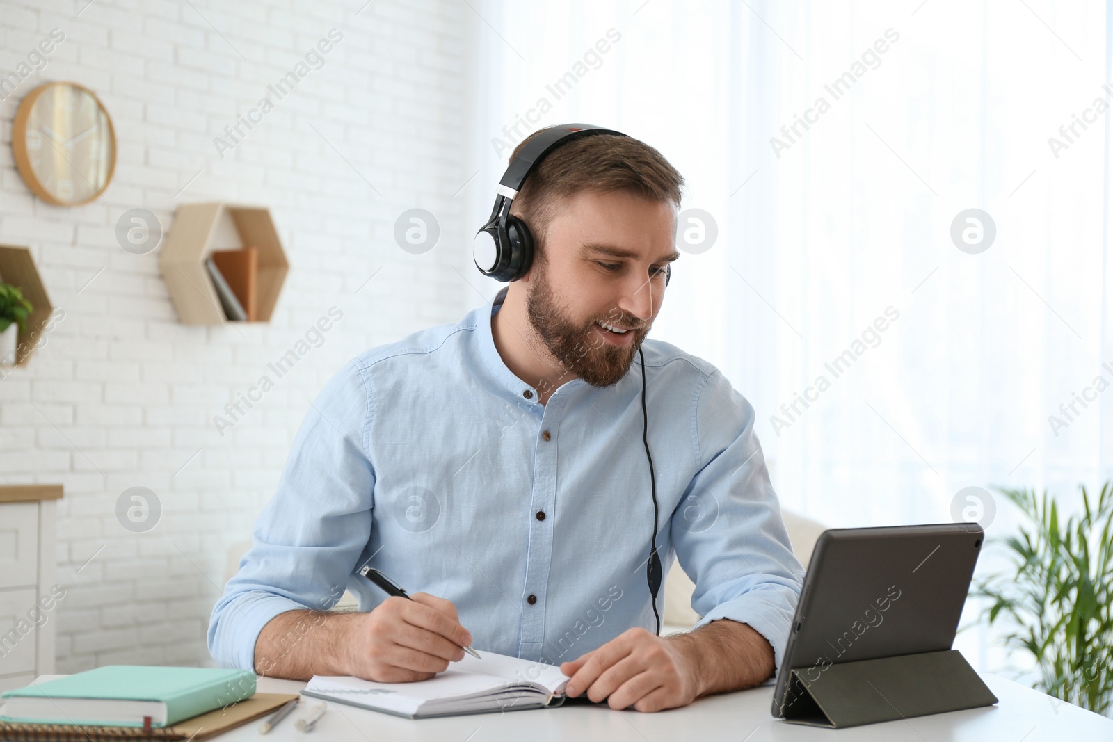 Photo of Young man taking notes during online webinar at table indoors