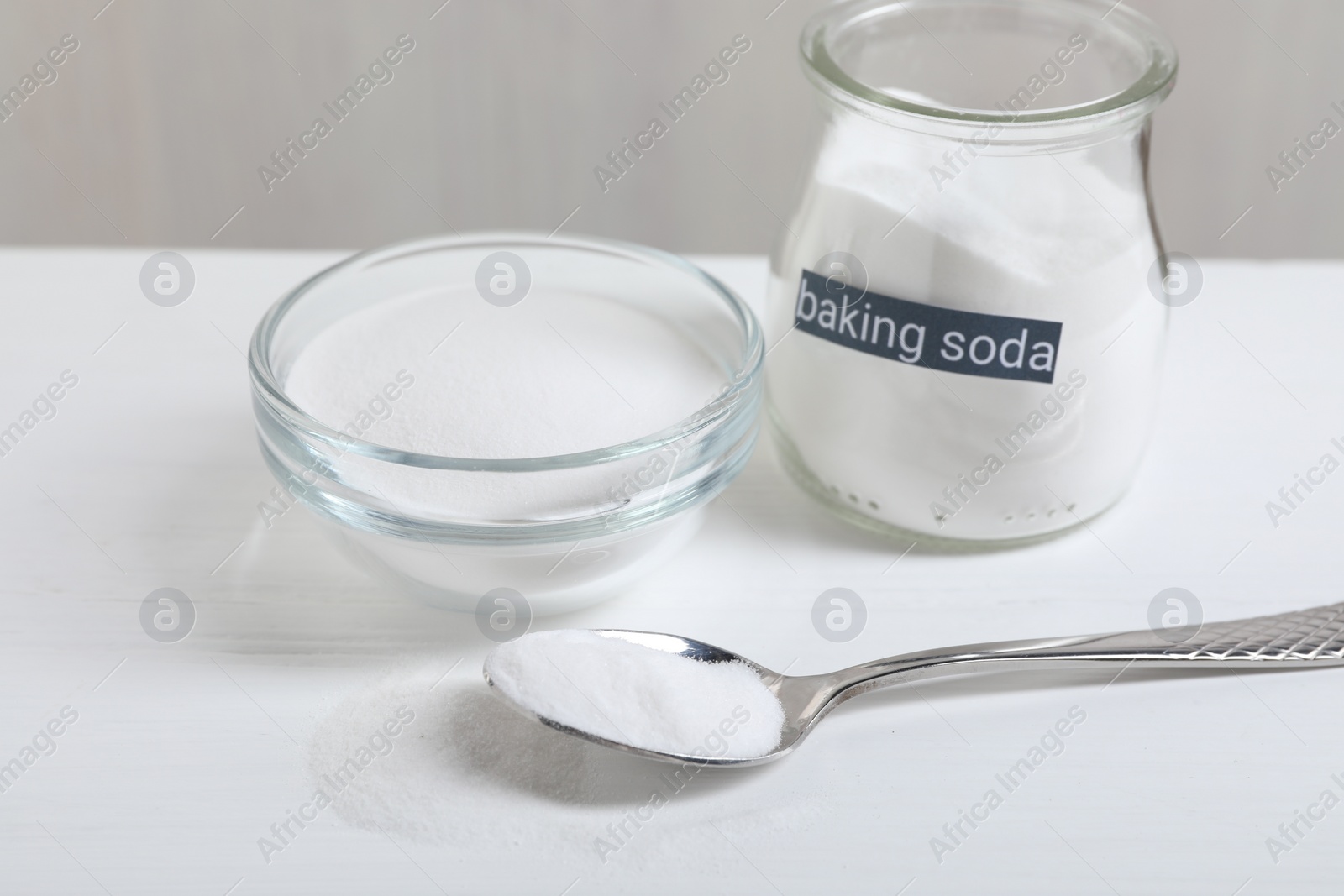 Photo of Baking soda in bowl, glass jar and spoon on white wooden table