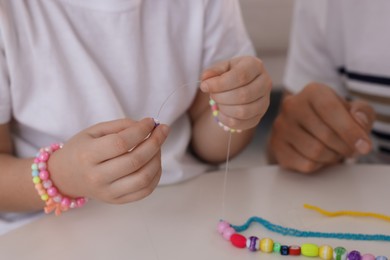 Photo of Father with his daughter making beaded jewelry at table, closeup