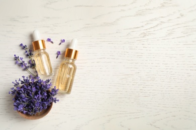 Flat lay composition with essential oil and lavender flowers on white wooden background. Space for text