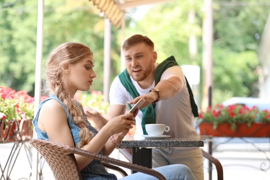 Photo of Young couple arguing while sitting in cafe, outdoors. Problems in relationship