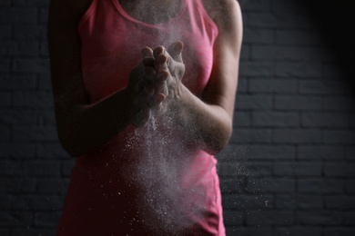 Photo of Young woman applying chalk powder on hands against brick wall