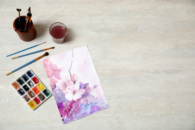 Photo of Flat lay composition with watercolor paints and floral picture on light table. Space for text