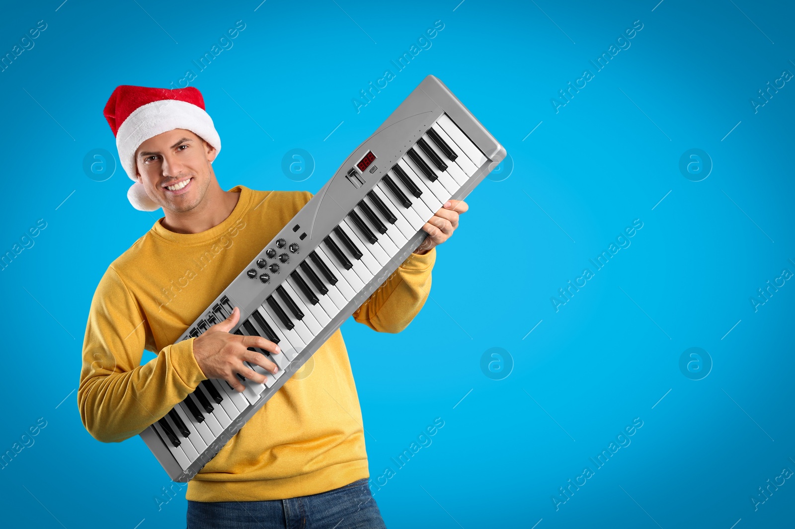 Photo of Man in Santa hat playing synthesizer on light blue background, space for text. Christmas music