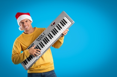 Photo of Man in Santa hat playing synthesizer on light blue background, space for text. Christmas music