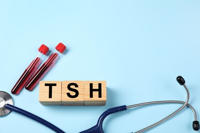 Photo of Endocrinology. Stethoscope, wooden cubes with thyroid hormones and blood samples in test tubes on light blue background. Space for text