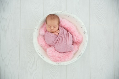 Photo of Adorable newborn girl lying in baby nest on light background, top view