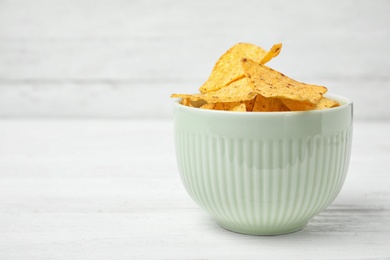 Bowl with tasty Mexican nachos chips on white wooden table, space for text