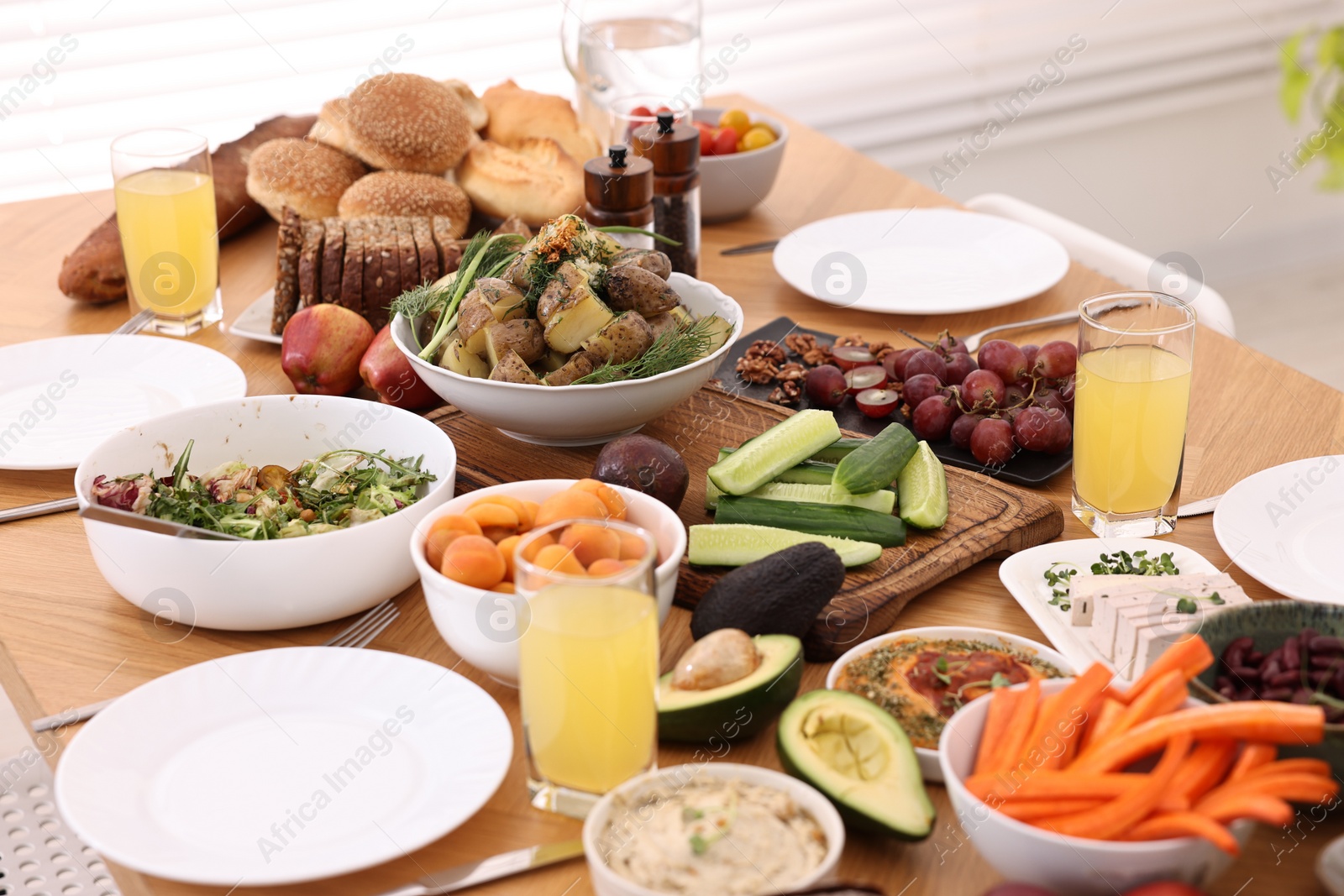 Photo of Healthy vegetarian food, glasses of juice, cutlery and plates on wooden table indoors