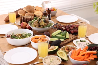 Healthy vegetarian food, glasses of juice, cutlery and plates on wooden table indoors