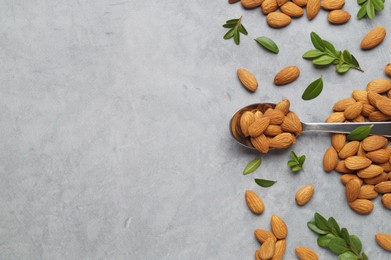 Spoon with tasty almonds and fresh green leaves on light grey table, flat lay. Space for text