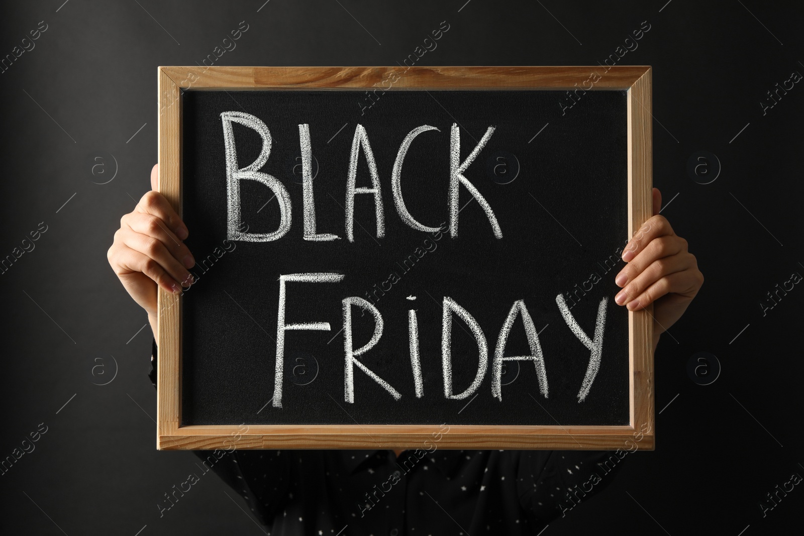 Photo of Woman holding chalkboard with words Black Friday against dark background