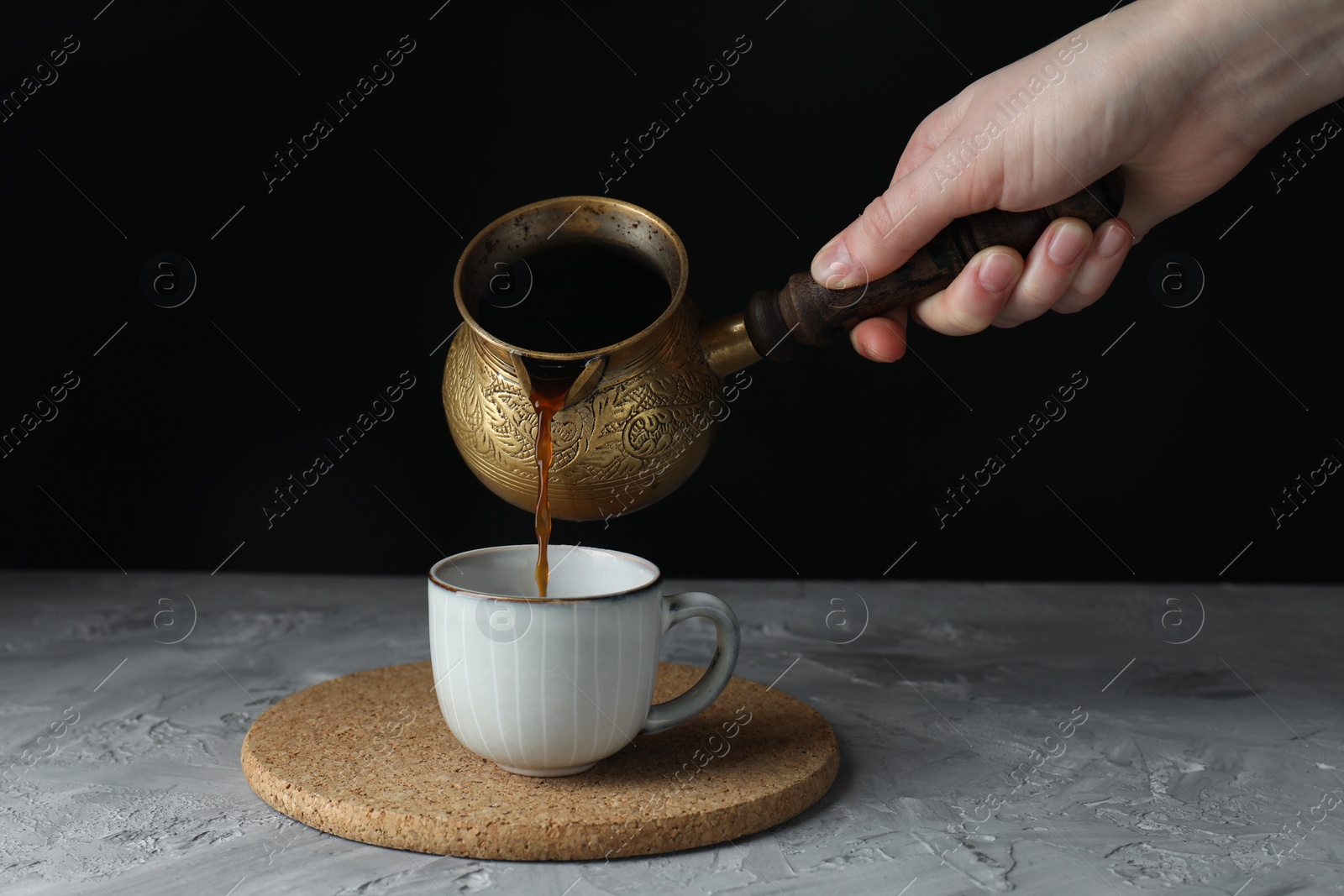 Photo of Turkish coffee. Woman pouring brewed beverage from cezve into cup at grey table, closeup