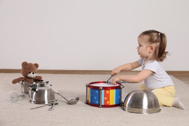 Photo of Cute little girl with cookware and toy drum at home