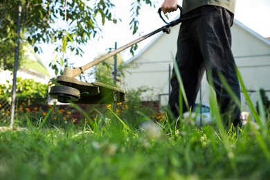 Photo of Man cutting green grass with string trimmer outdoors, closeup