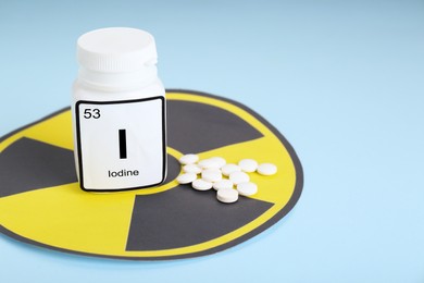Photo of Bottle of medical iodine, radiation sign and pills on light blue background. Space for text