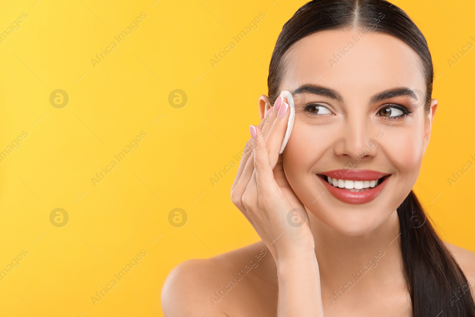 Photo of Beautiful woman removing makeup with cotton pad on orange background, space for text