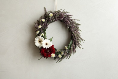 Photo of Beautiful autumnal wreath with heather flowers hanging on light grey background. Space for text